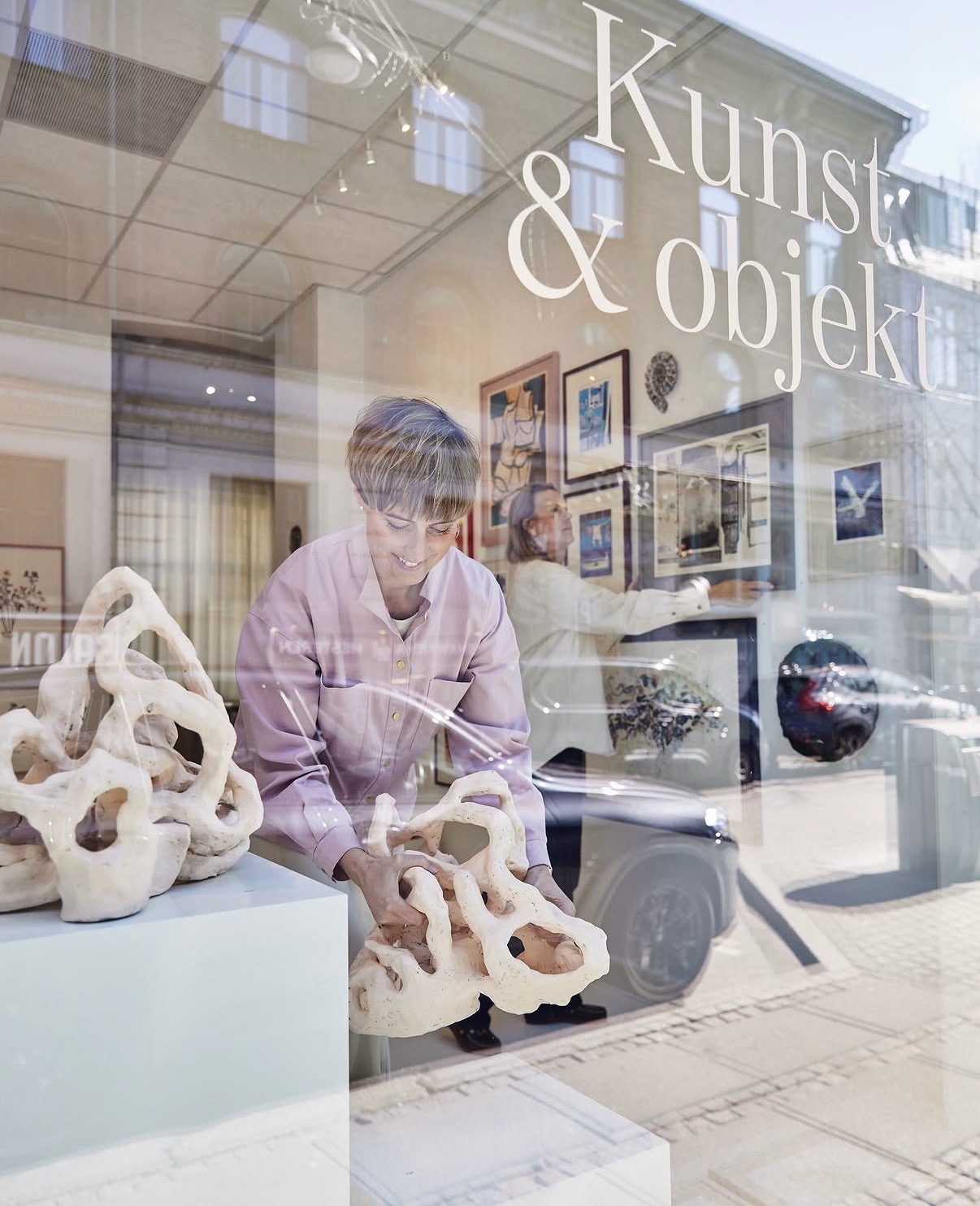 Kunst & Objekt storefront window with the gallery owner arranging ceramic sculptures